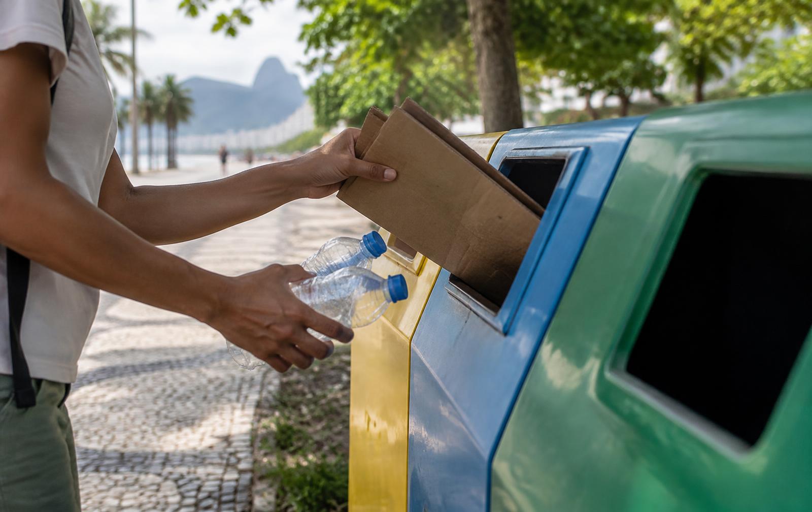 Pessoa descartando papelão e garrafas plásticas em um contêiner de coleta seletiva